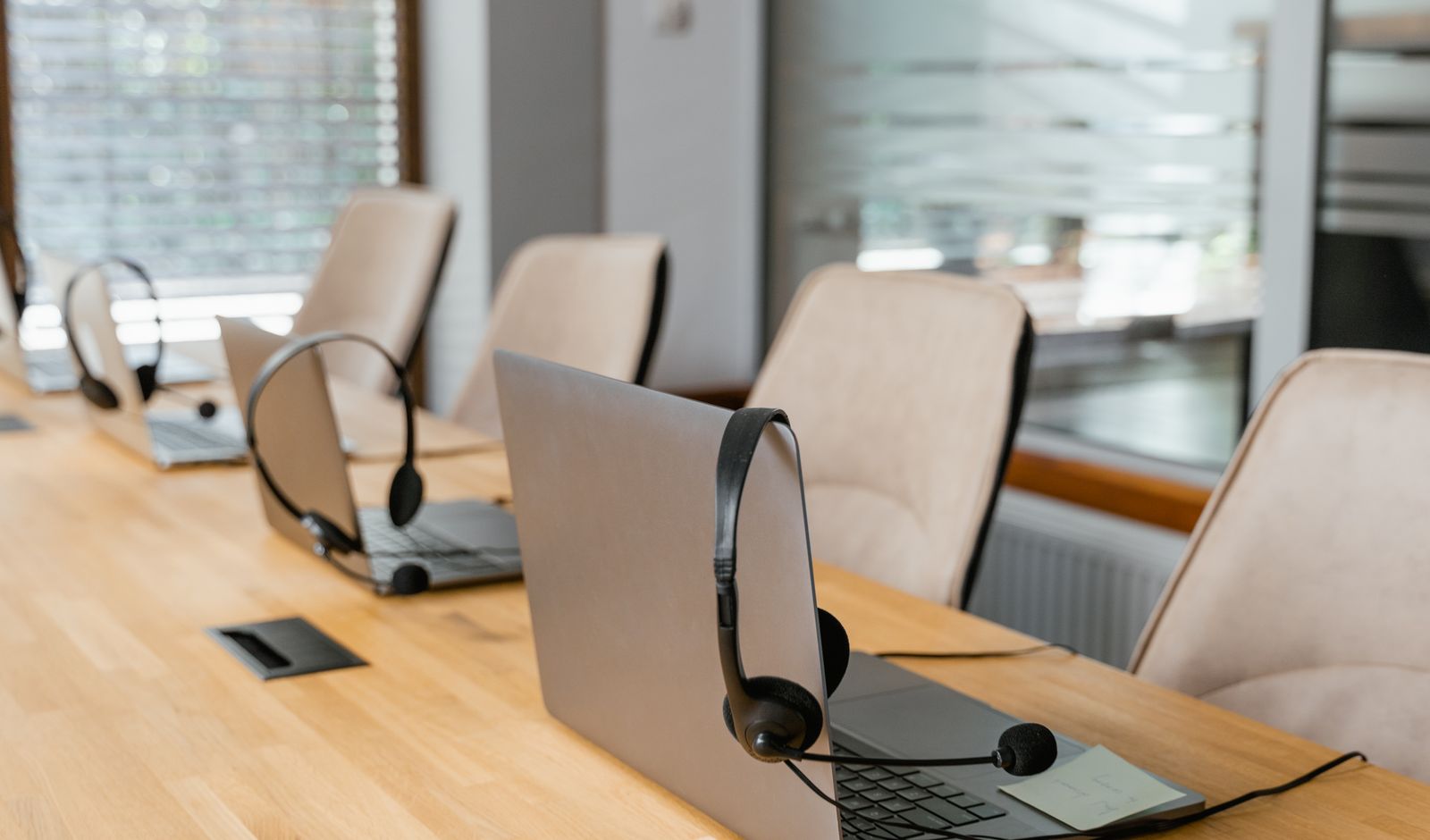 A row of empty desks with laptops and headsets waiting in an office