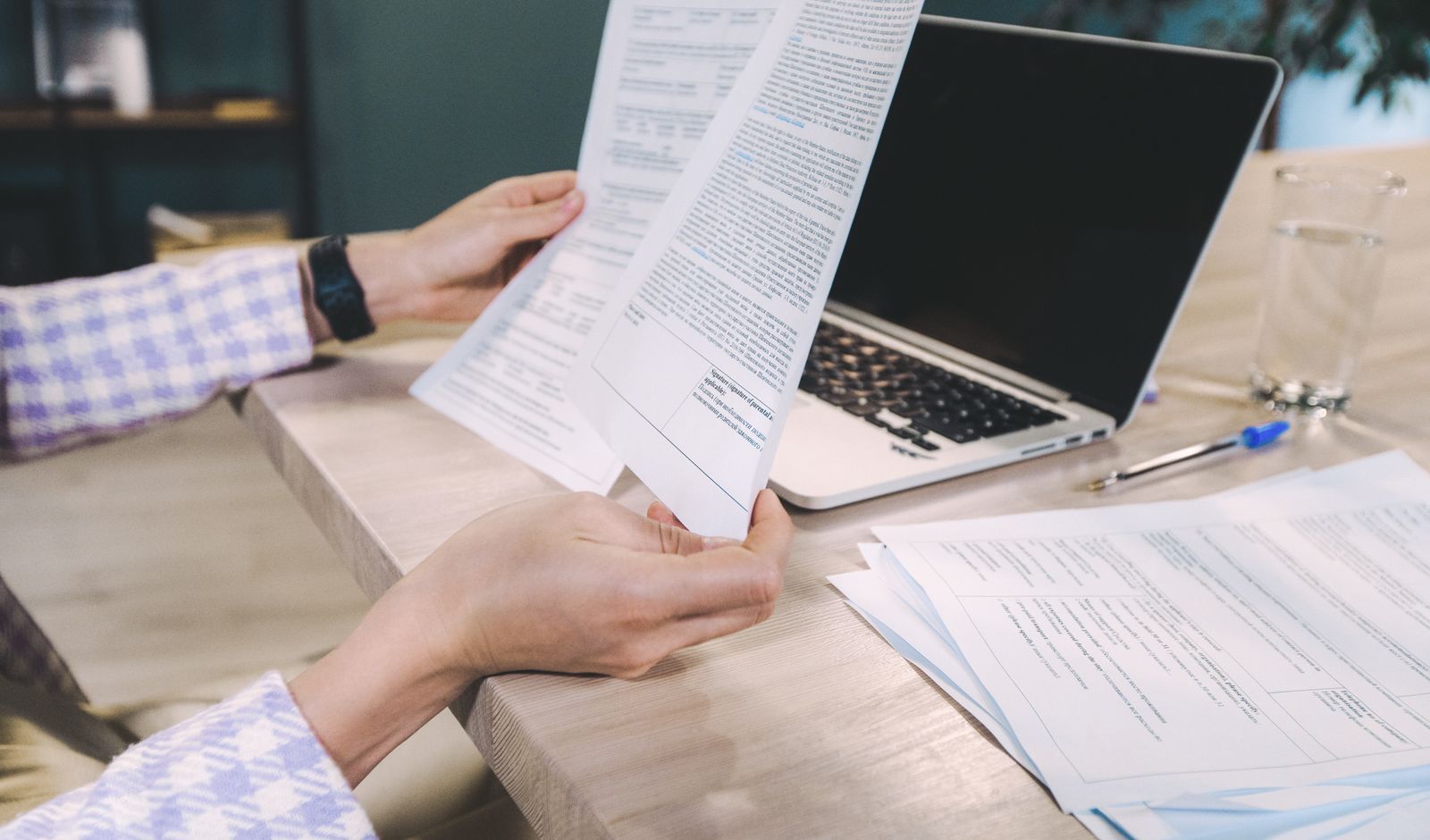 Hands checking a printed report against papers spread beside a laptop