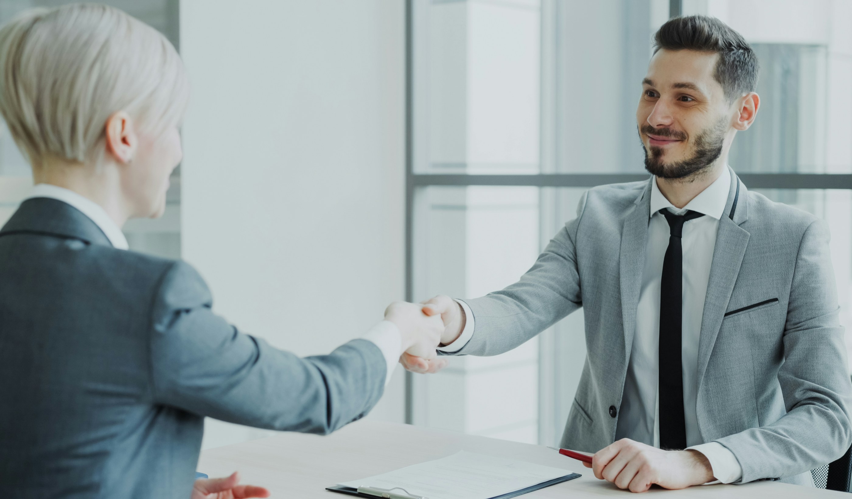 Two professionals shaking hands across a table in an office