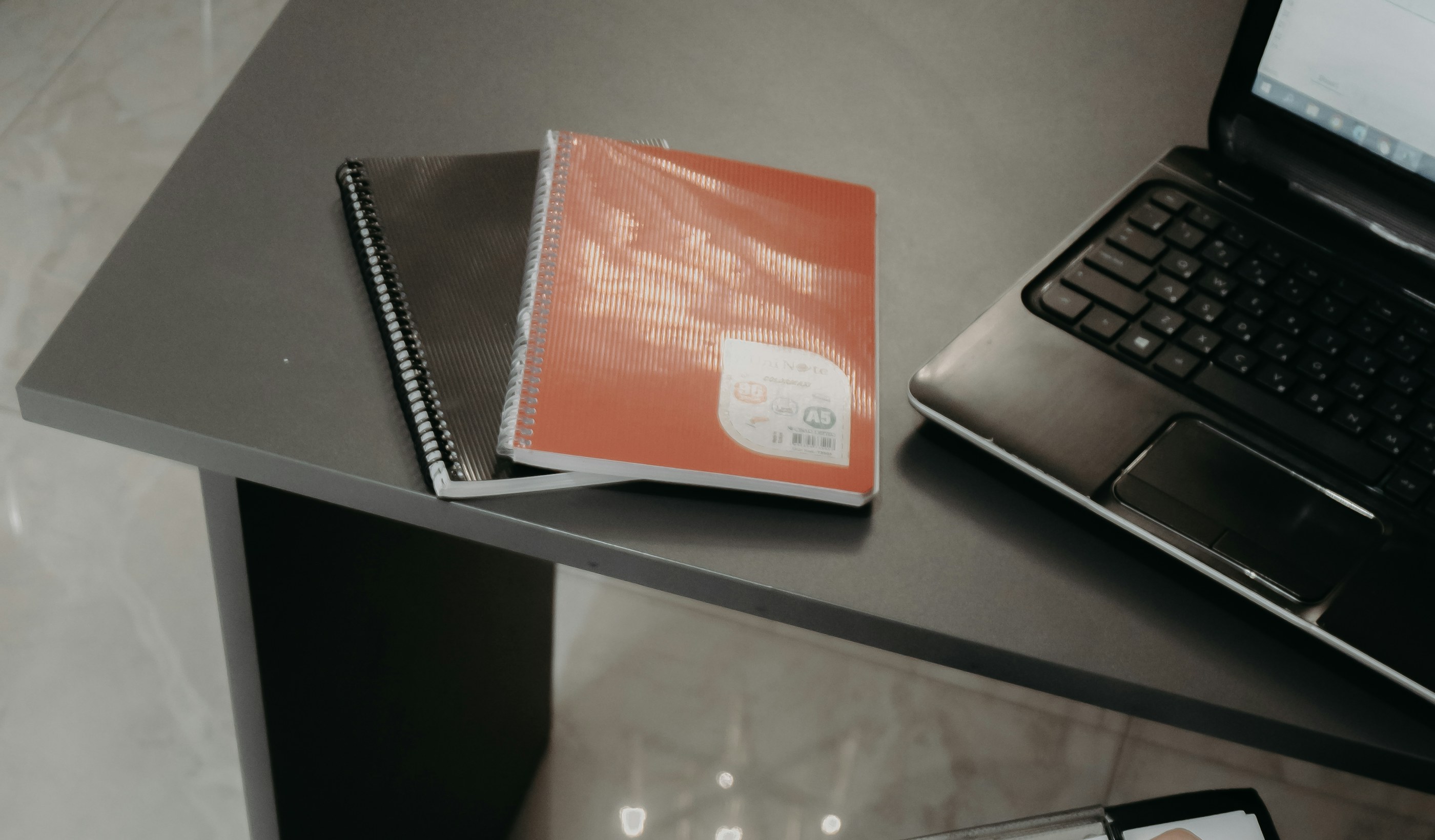 Someone writing notes on a clipboard at a desk beside a laptop