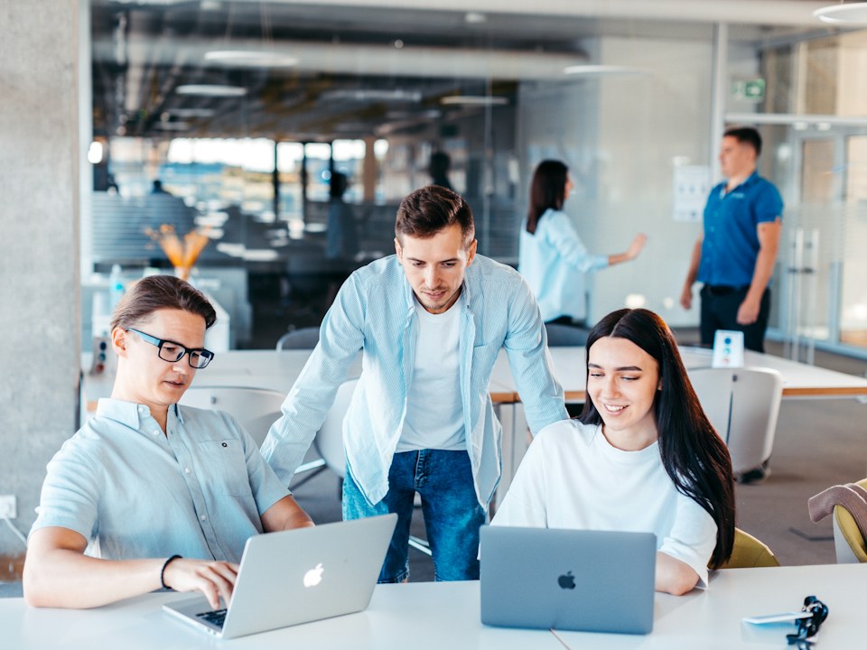 A group of colleagues looking at laptops together in a bright office