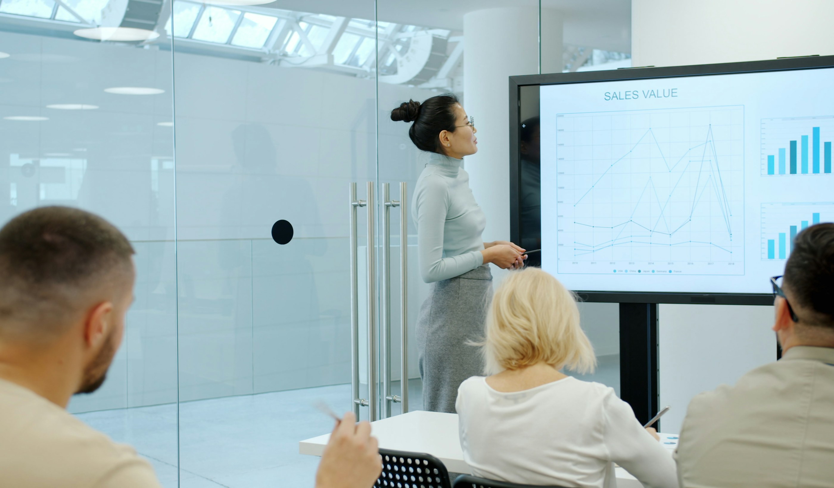 A colleague presenting charts on a large screen to two people in a meeting room