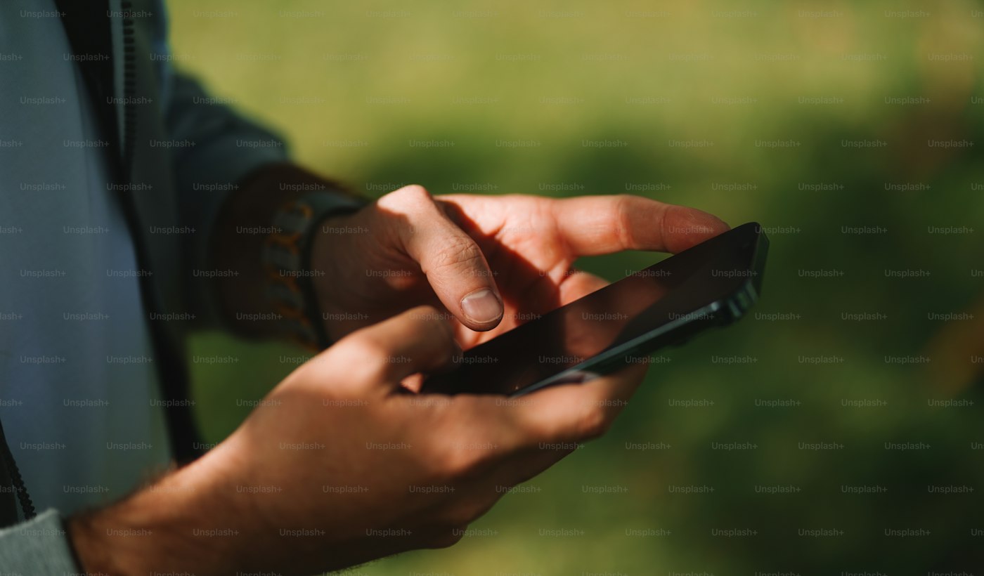 A close-up of two hands holding and using a smartphone outdoors