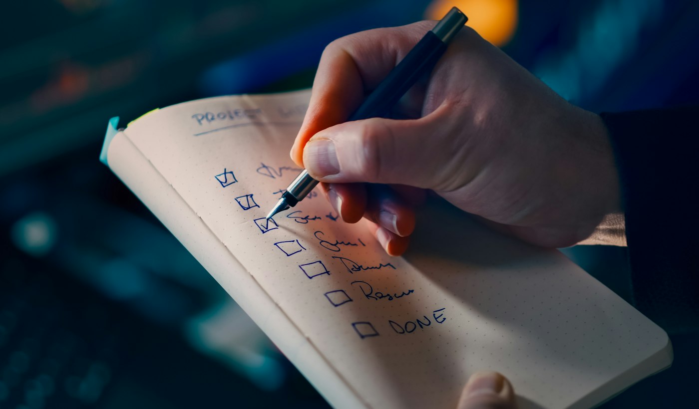 A hand ticking off items one by one on a handwritten checklist