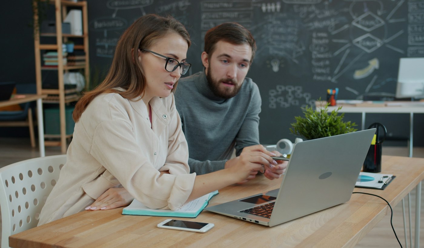Two colleagues comparing results on a laptop screen in an office