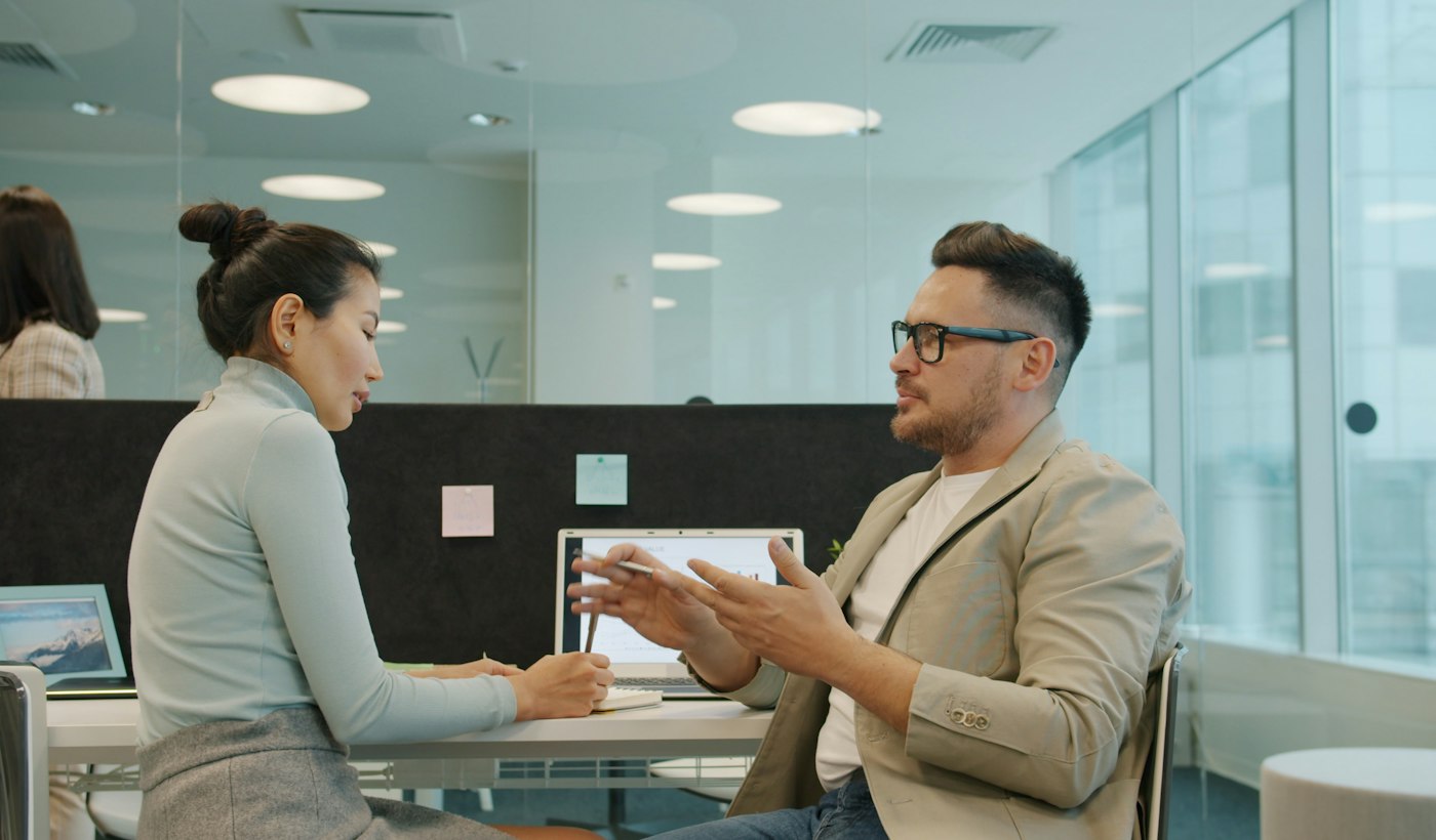 Two colleagues discussing work across a desk in a modern office