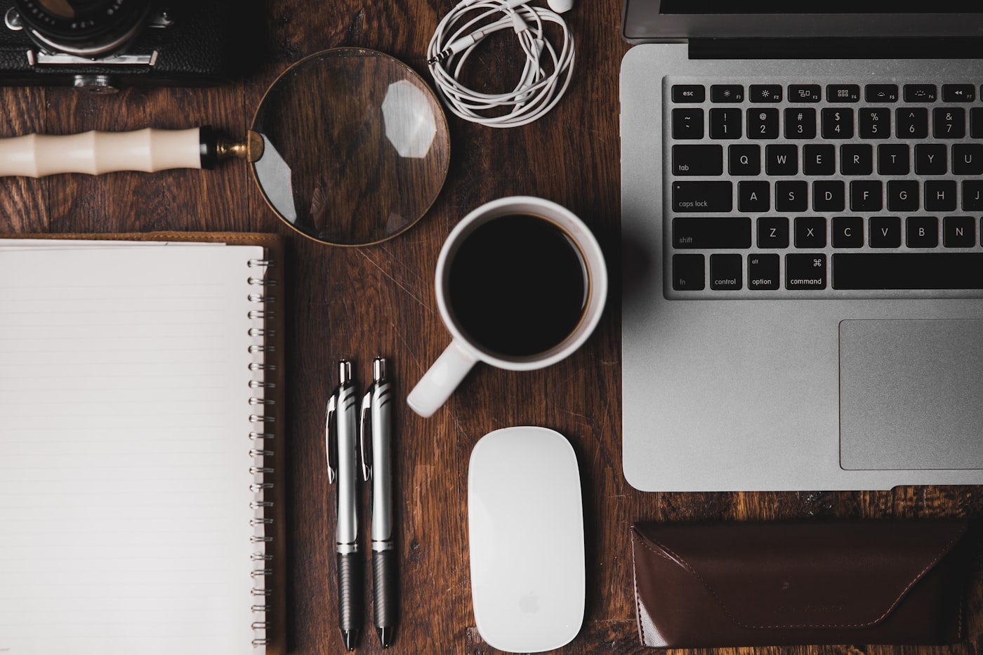 A desk from above with a notebook, pens, coffee and a laptop